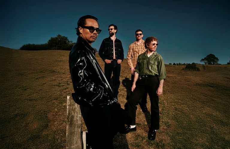 Promotional portrait of Australian indie rock band The Temper Trap posing outdoors on a grassy hill.